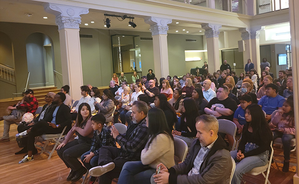 Families and students sit theatre style in historic venue.