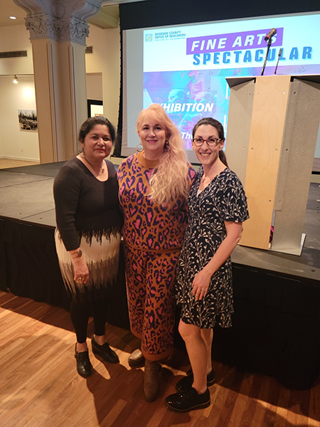 Three women stand by Fine Arts Spectacular Stage