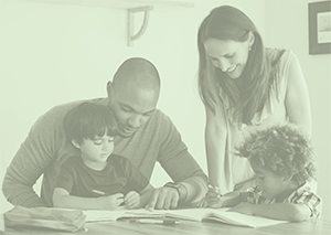 Parents helping to focus two young children on the books at the table in front of them