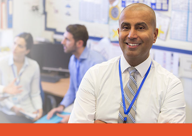 Man smiles confidently while adult students are engaged in conversation behind him