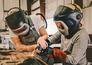 Adult helping student in welding shop