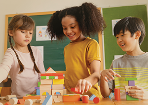 Three young students in classroom working with blocks