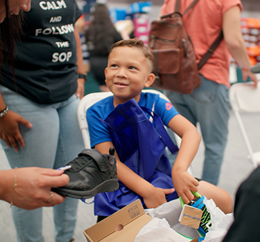 Young boy smiling as he tries on a pair of shoes and other pair is offered to him