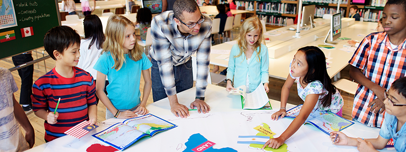 Elementary students with teachers studying world countries in school library