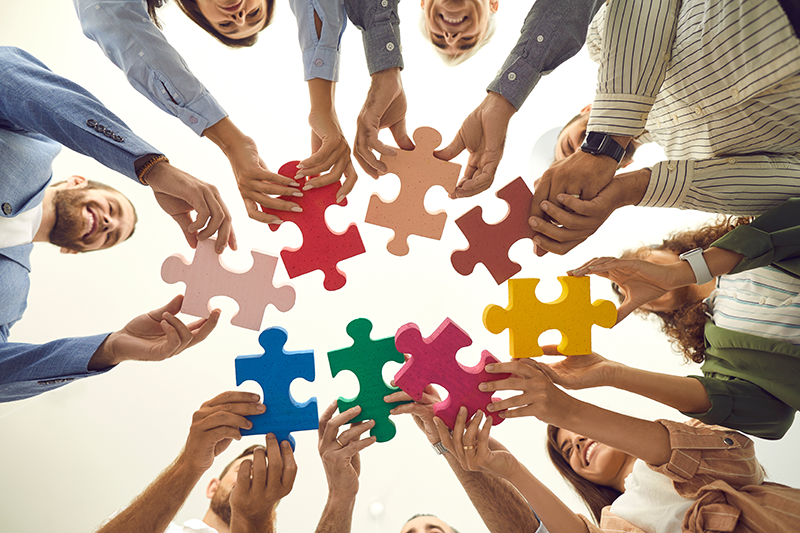 Team of adults holding large puzzle pieces forming a circle