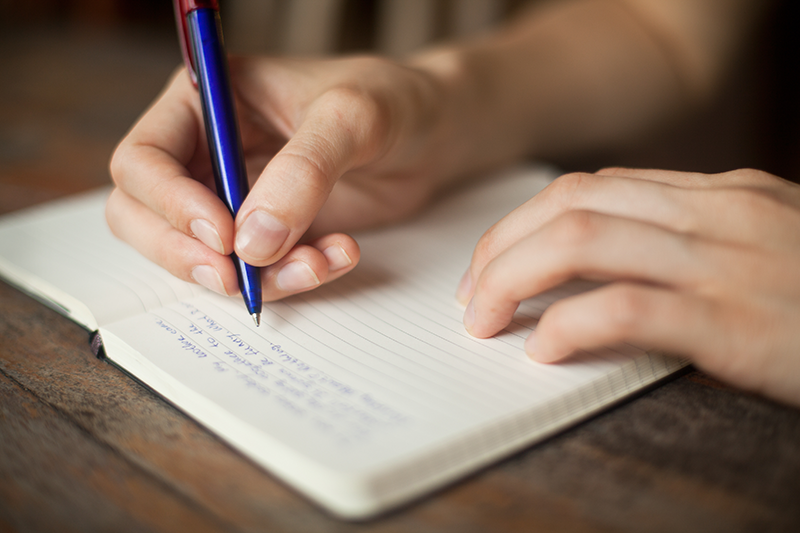 a person's hands writing in a journal