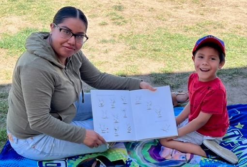 Woman sits with young boy who shows off open book with excitement